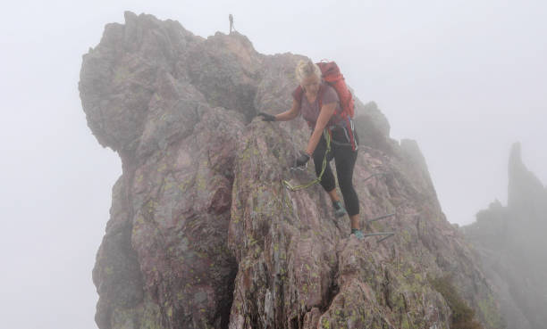 mature woman moves along rocky ridge on a via ferrata in the fog - climbing rock climbing rock mountain climbing imagens e fotografias de stock