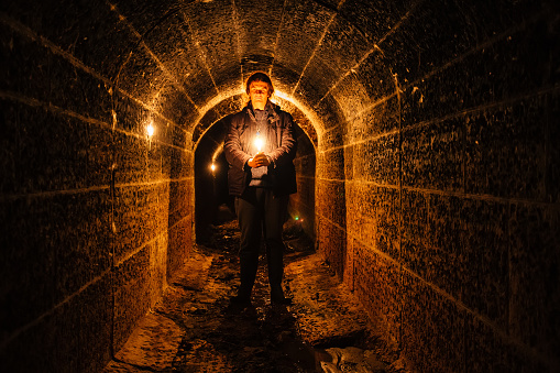 Urban explorer with candle in old vaulted underground tunnel.