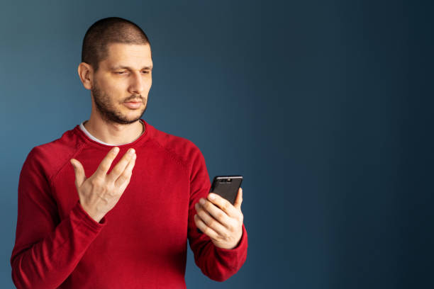 istock Caucasian man wearing red sweater standing in front of the blue background wall using smart phone mobile to make a video call or as blog or blogger talking gesturing with hand 1208915712