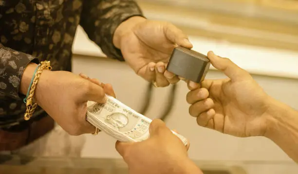 Photo of Close up of hands buying or purchasing gold jewellery by paying Indian currency at jewelry shop India - concept of gold investment for profit