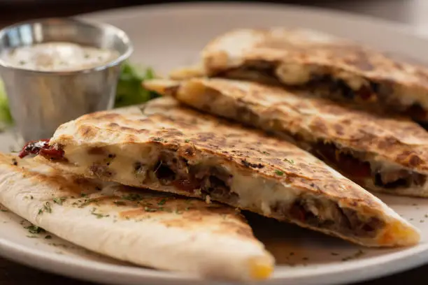 Selective focus steak quesadilla with Monterey Jack cheese, jalapeños, red chiles, and onions with sour cream on the side.