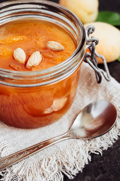 homemade apricot jam with apricot kernels in glass jar on black table. homemade jam preserves - preserves jar apricot marmalade imagens e fotografias de stock