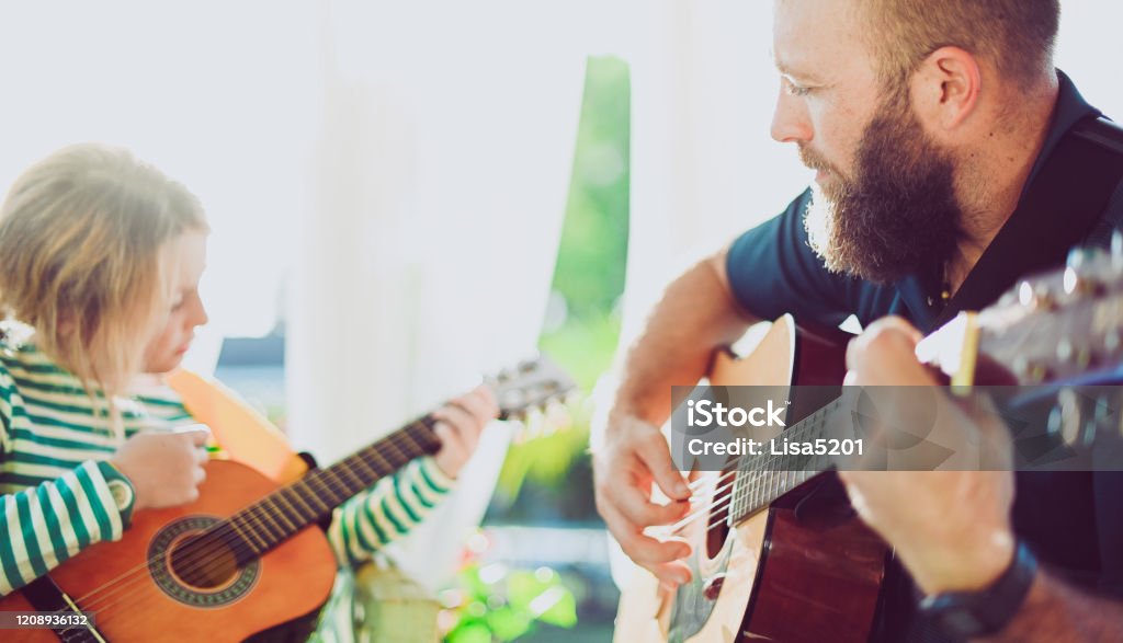 Jam session man and child play guitar Man and girl play guitar outdoors with dreamy sunflare. Man is father or guitar teacher, girl is 8 years old, elementary age. They are playing guitar together in a heartwarming jam session. Father and daughter using musical instruments together Music Therapy Stock Photo