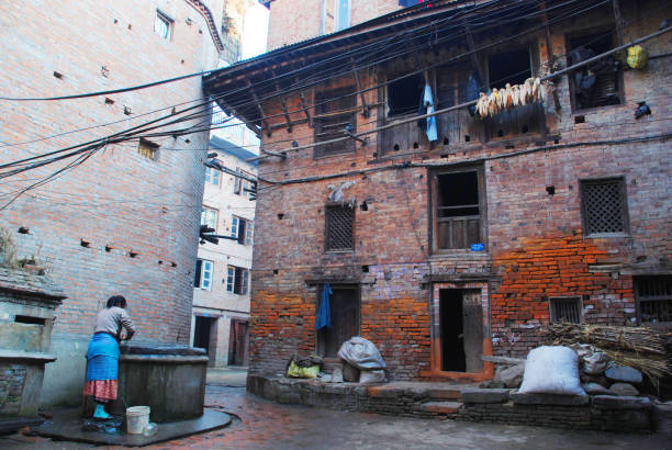 A nepali woman collecting water from the community well outside their house during winter afternoon time, at old town of Kathmandu.
