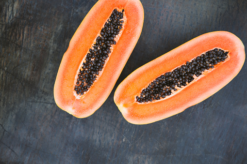 Whole papaya fruit and half with seeds on wooden background