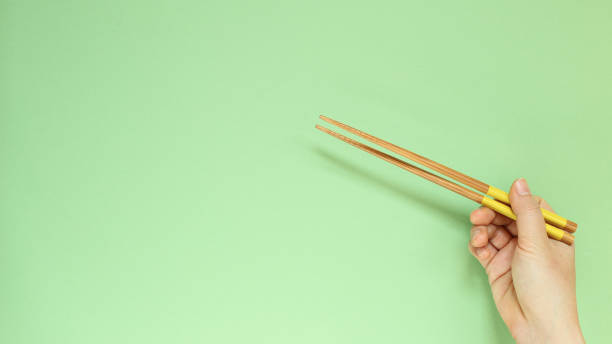 istock Hand holding wooden chopsticks isolated on green background. copy space 1208971679
