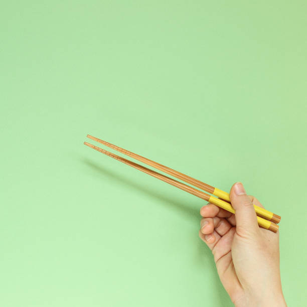 istock Hand holding wooden chopsticks isolated on green background. copy space 1208971711