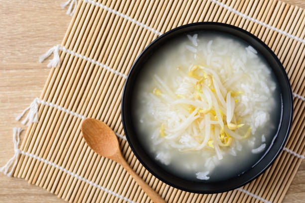 Rice soup with mung bean sprouts in a bowl and wooden spoon on bamboo sheet, Asian vegan food