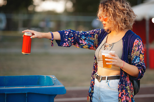 Young woman recycling beer can at outdoor music festival
