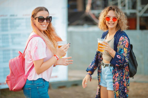 mulheres jovens sorridentes com copos de cerveja em festival de música ao ar livre - outdoors drinking women friendship - fotografias e filmes do acervo