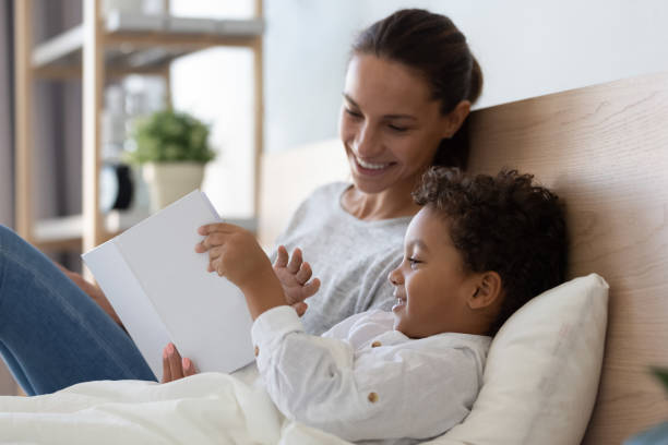istock Mixed race family lying on pillows in bed, holding book. 1208979486