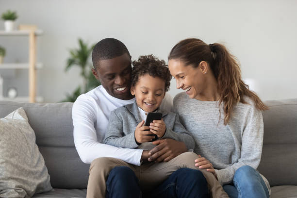 istock Happy black husband holding son on knees, playing on phone. 1208979523