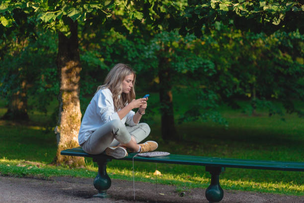 istock Carefree young woman text messaging on her mobile phone while sitting on the bench 1208985917