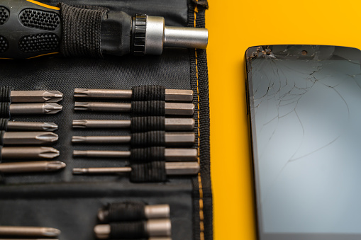 Smartphones with damaged screen and screwdriver with bits,  yellow background. The scene is located in a studio environment. The footage is taken with Sony A7III camera