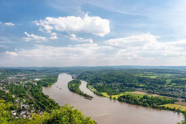 River Rhein in western Germany flowing along the city against the sky with clouds. Visible barges and ships on the river.