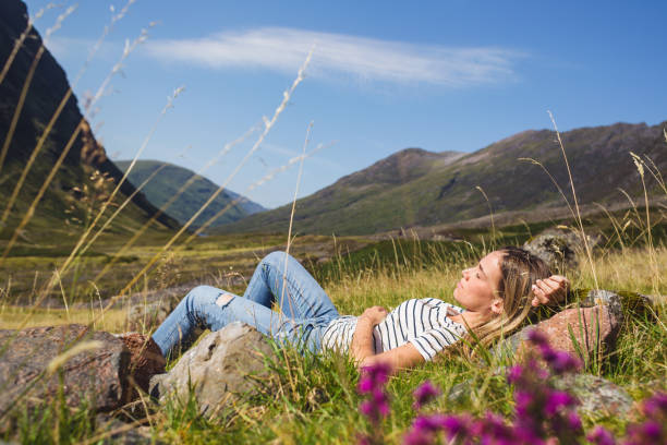 Beautiful young female tourist spending beautiful sunny day in nature, at Highland in Scotland while lying on the grass