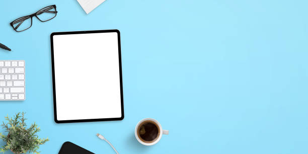 istock Tablet mockup on blue work desk with plenty of space for text. Top view, flat lay scene with up of coffee, keyboard, glasses and plant 1208989454