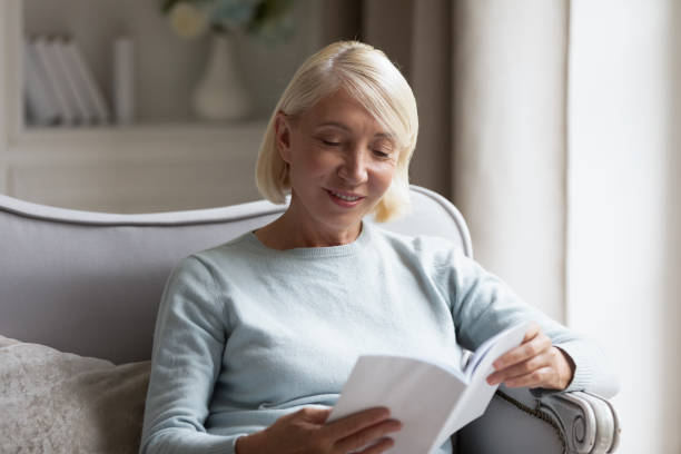 istock Middle-aged mature woman reading interesting book at home 1208992056