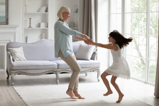 Energetic grandmother have fun dancing with little granddaughter Happy middle-aged grandmother play dancing and swirling in living room with cute little granddaughter, energetic senior granny have fun engaged in childish funny activity with small preschooler child grandmother stock pictures, royalty-free photos & images