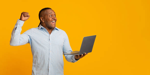 istock Excited african middle aged man with laptop cheering his win 1208994002