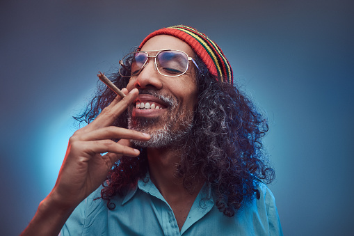 African Rastafarian smokes weed and gets high. Isolated on a blue background.