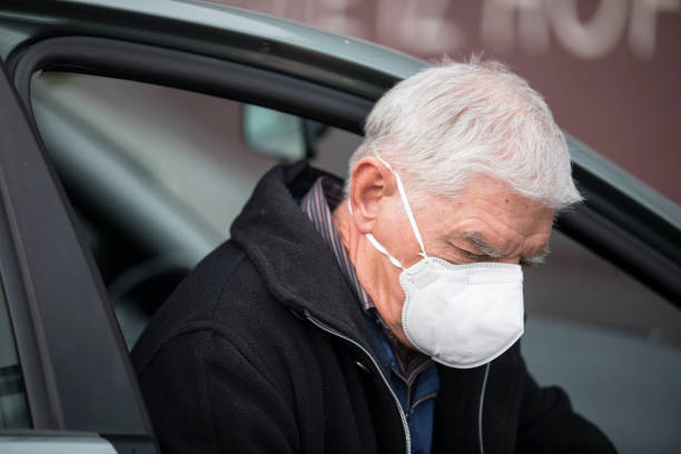 senior adult man getting out of his car wearing protective face mask - stock photo - illness mask pollution car imagens e fotografias de stock