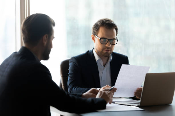 istock Serious businessman reading cv new job candidate and using laptop. 1208998441