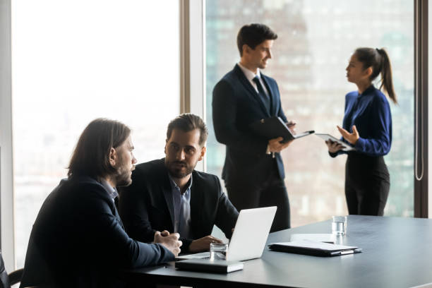 istock Two handsome businessmen in suits talking on colleagues background. 1208998515