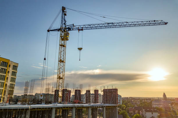 istock Apartment or office tall building under construction. Brick walls, glass windows, scaffolding and concrete support pillars. Tower crane on bright blue sky copy space background. 1208999757