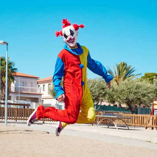 Photo of scary clown jumping outdoors