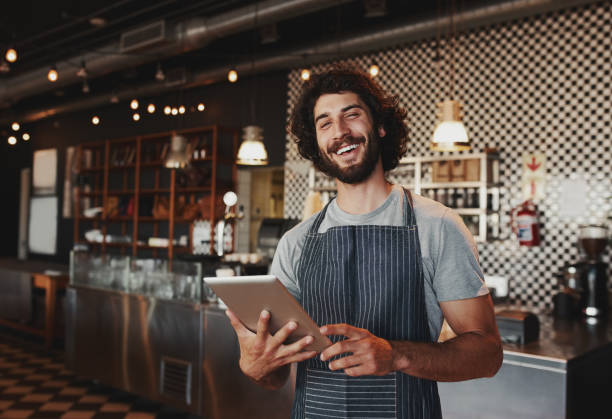 istock Handsome young caucasian coffee shop owner wearing apron laughing using digital tablet 1209000712