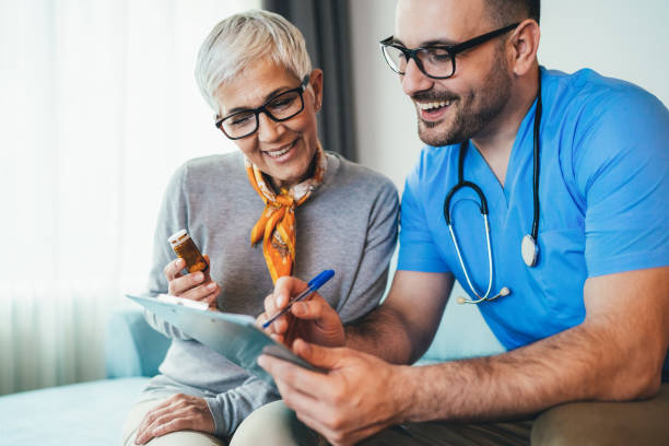 Young doctor and senior woman Young smiling doctor is consulting a modern senior woman - patient, on the visit at home old woman smiling tablet stock pictures, royalty-free photos & images