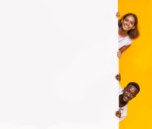istock Afro boy and girl looking from behind advertising board 1209004607