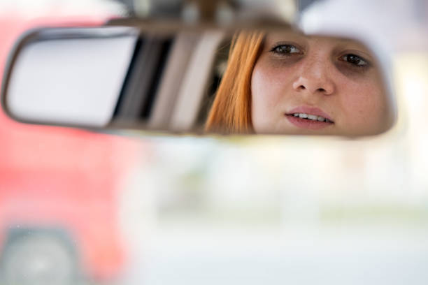 istock Young woman driver checking rear view mirror looking backwards while driving a car. 1209006523