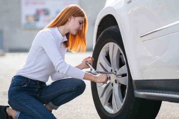 istock Young woman with wrench changing wheel on a broken car. 1209006563