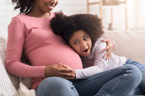 Photo of Excited little girl touching and listening to her pregnant mother's belly