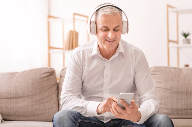 istock Elderly man listening to music sitting on sofa 1209007911