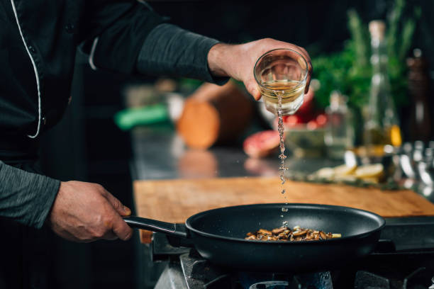 Chef Pouring White Wine into Frying Pan with Sliced Shiitake Mushrooms stock photo