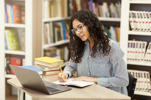 istock Confident latina girl sitting at desk in modern library 1209008621