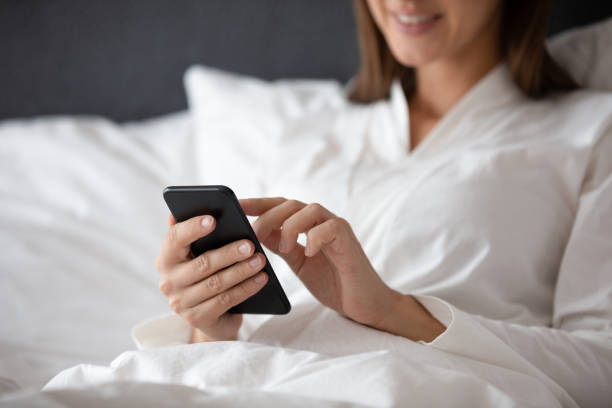 istock Close up smiling woman using phone, sitting in bed 1209008660