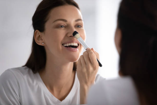 istock Smiling woman looking in mirror, applying makeup with brush 1209008743