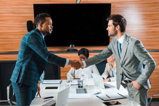 istock two handsome businessmen shaking hands while standing near multicultural colleagues in conference hall 1209011975