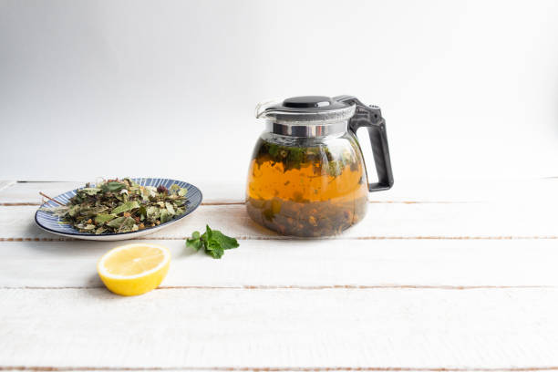 Glass transparent tea pot  with brewed forest herbs, mint, lemon   on rustic wooden background