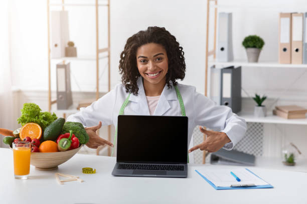 istock Cheerful black woman dietologist pointing at empty laptop screen 1209014400