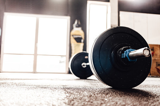 Set of heavy barbells sitting on a gym floor with a sun flare coming through the window