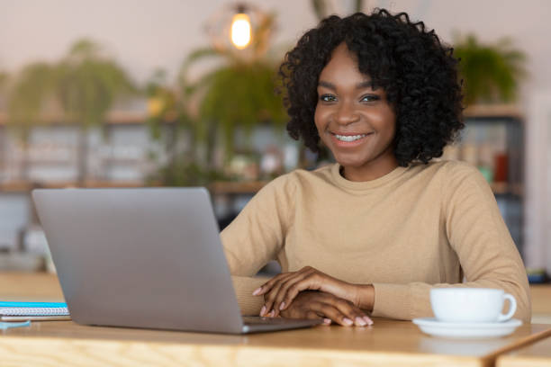 istock Afro girl smiling at camera while working online at cafe 1209014863
