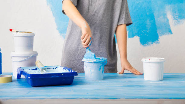 istock Paint on table. Girl dips a brush in a bucket. 1209015026