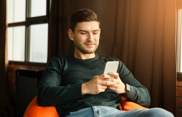 istock Student Using Phone Texting Sitting In Beanbag Chair Indoor 1209016337
