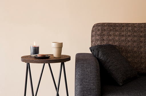 Detail view of modern round wood metal coffee table with cappuccino mug, glass candle burning by the side of sofa.