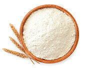 Flour in a wooden plate and wheat spikelets on a white. The view from the top